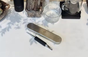 Metallic device with a pen on a white surface with water in the background